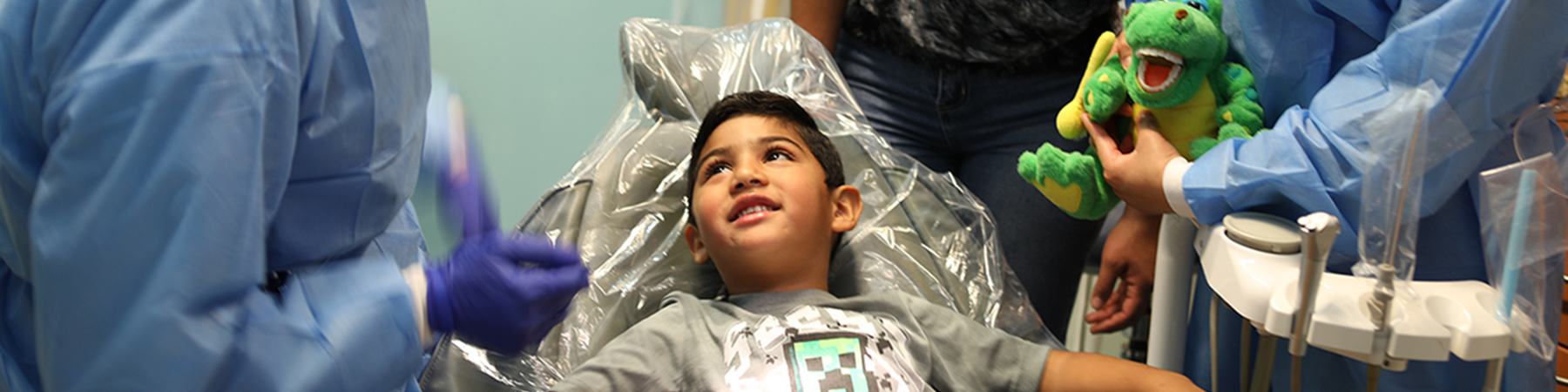 Dental clinic kid patient visit Boy smiling in dentist chair looking up at team of dentists