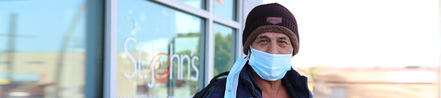 Man with a mask and hat standing outside St. John's health clinic